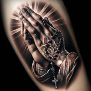 Praying hands in grayscale with rosary beads and cross pendant on a dark sleeve; black and grey cover-up tattoo project.