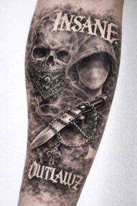 Black and grey tattoo design on forearm featuring a skull and hooded figure; project idea, perfect for a cover-up.