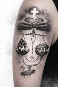 Black and grey tattoo design concept showing a balance scale with a cross atop, hands holding the beam, and dangling chains and pans; project idea.