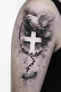 Bold black and grey tattoo design of a cross with rosary beads and a dove, presented as a project idea.